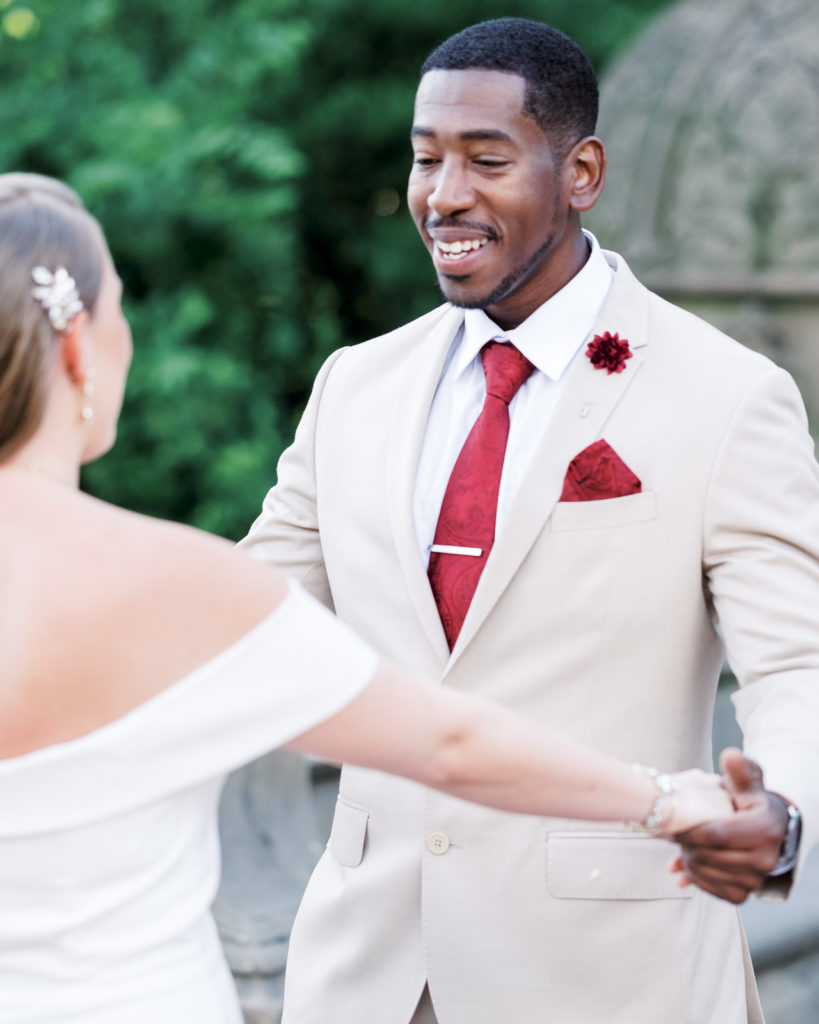 The groom holds hands with the bride and gives her a look of love at Bethesda Terrace and fountain moments after their first look.