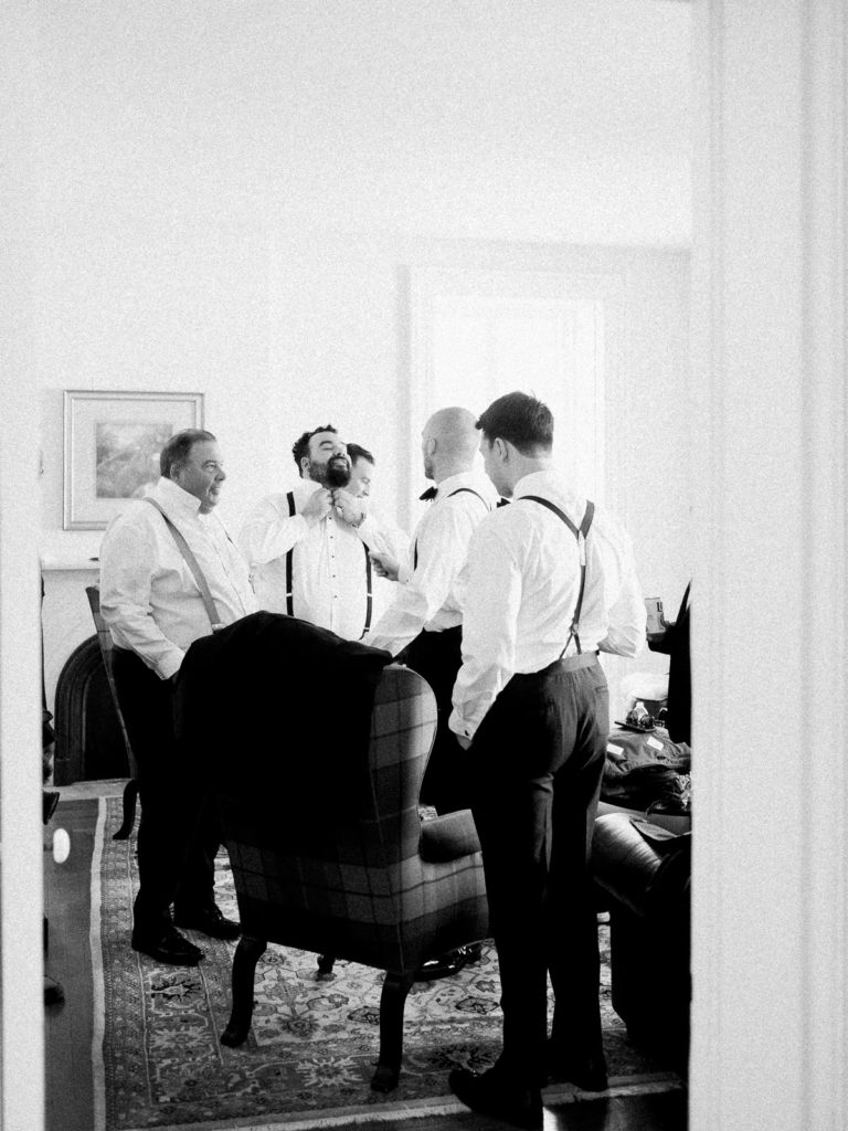 A far away image of the groom and all of his groomsmen getting ready in the groom's suite at Brecknock Hall.