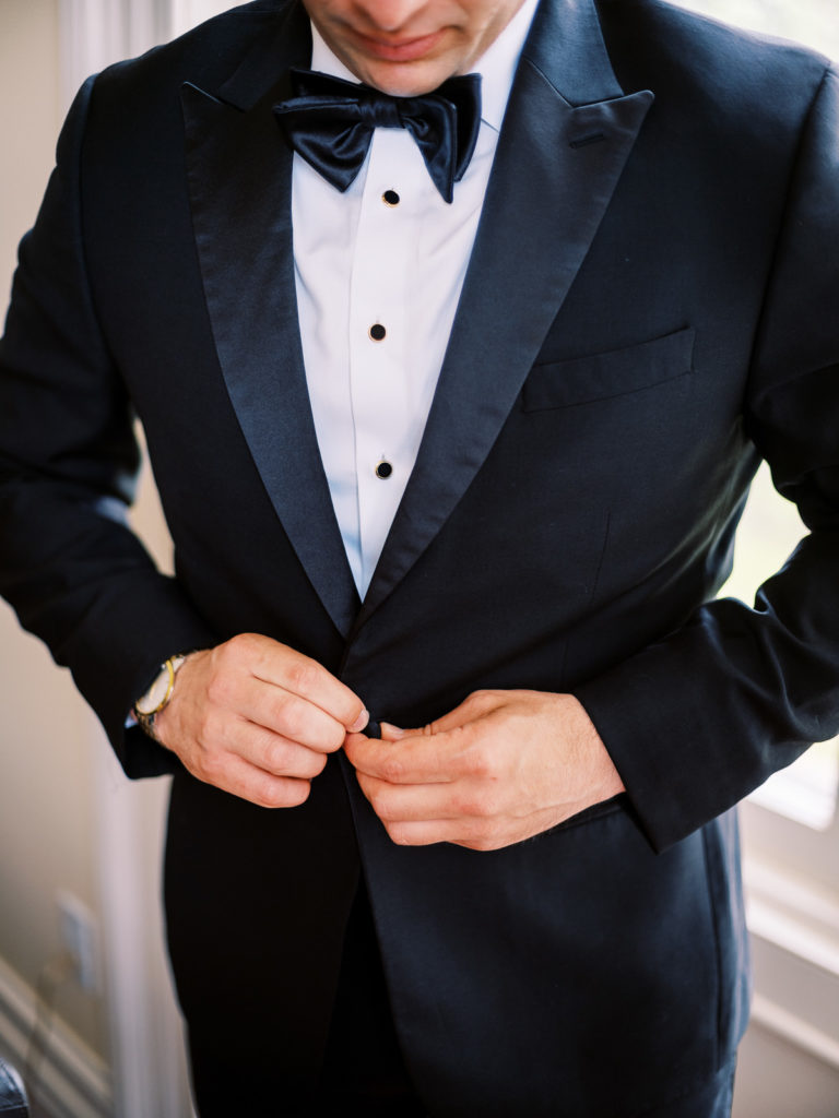 The groom buttons his The Black Tux tuxedo.