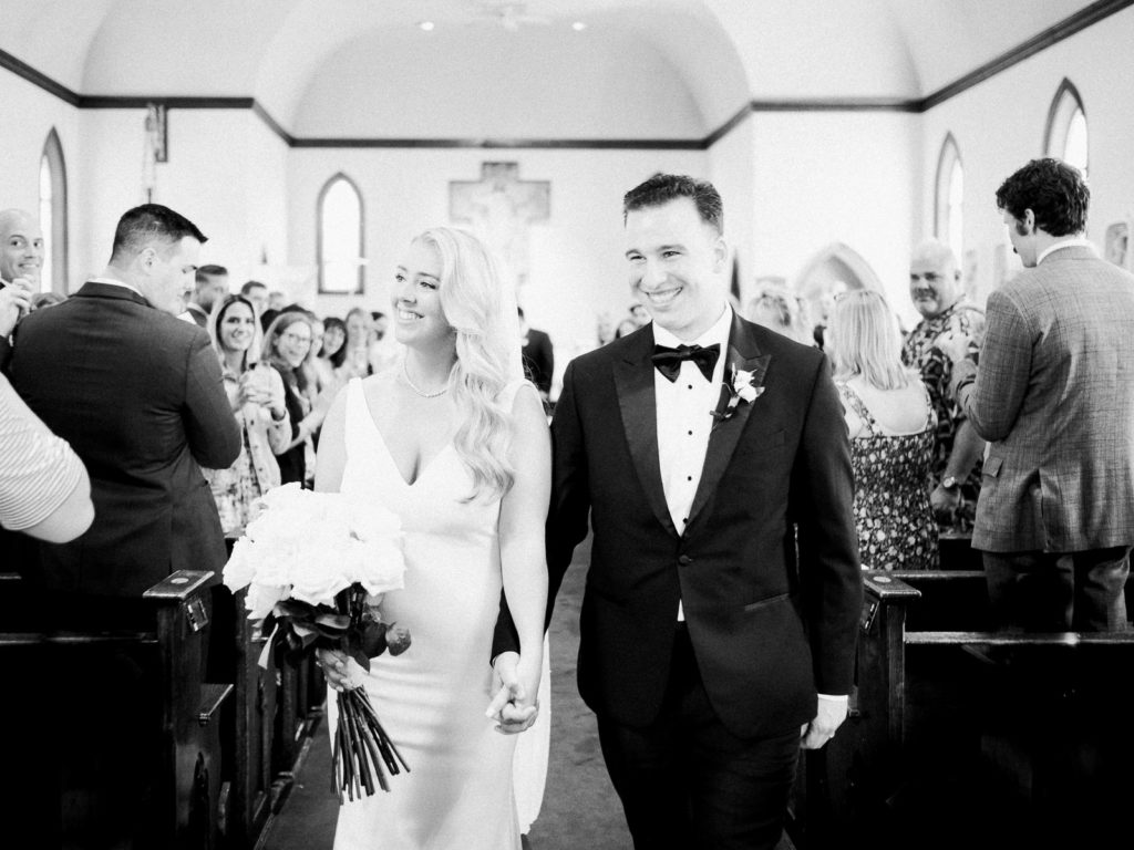 The bride and groom, wearing pronovias and The black Tux holding flowers by Kim Jon Designs walk down the aisle right after being married!