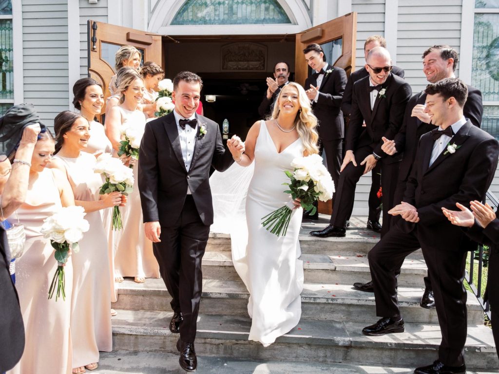 The bride and groom wearing pronovias and The Black Tux with flowers by Kim Jon Designs walk down the steps and are greeted by their loved ones!