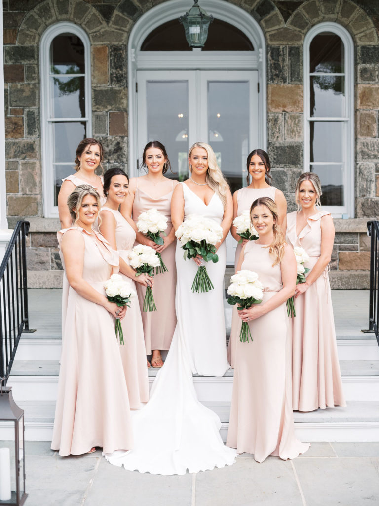 The bride dressed in pronovias and her bridesmaids wearing BHLDN pose outside the steps holding flowers made by Kim Jon designs during their Brecknock Hall Wedding.