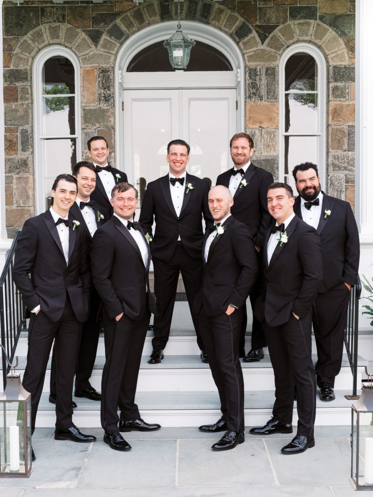 The groom and his groomsmen wearing The Black Tux pose on the steps during their Brecknock Hall Wedding.
