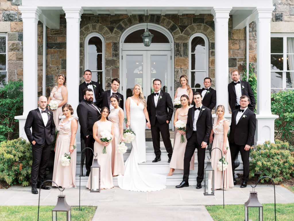 The bride and groom wearing pronovias and The Black Tux with flowers by Kim Jon designs pose vanity fair style with their wedding party during their Brecknock Hall Wedding. The bridesmaids are wearing BHLDN dresses.