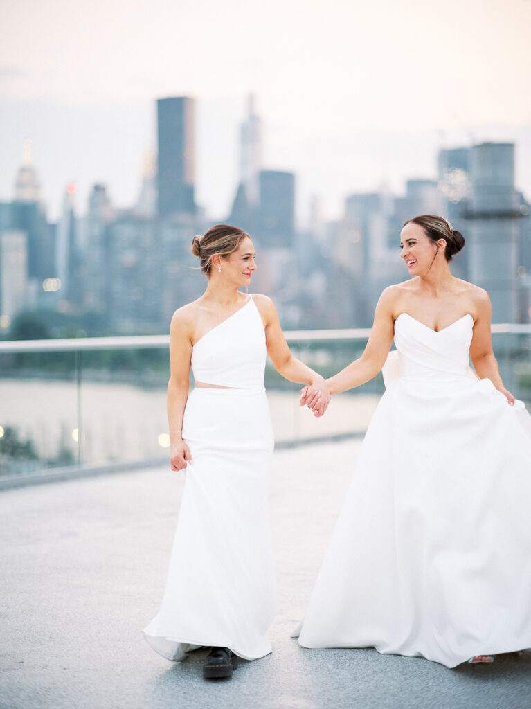 Two brides walking with NYC skyline in background.