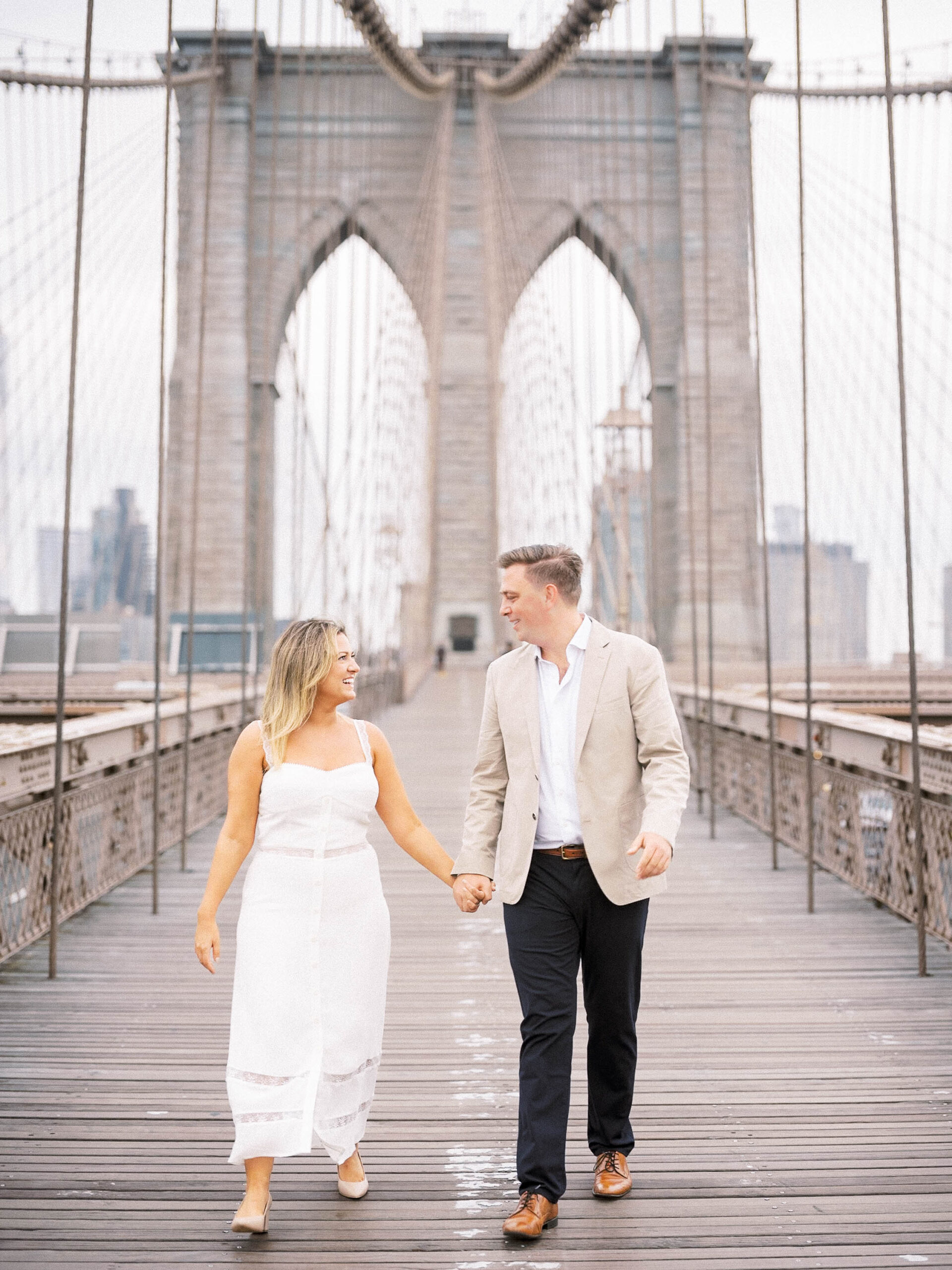 Couple walks on brooklyn bridge in dumbo during engagement session.