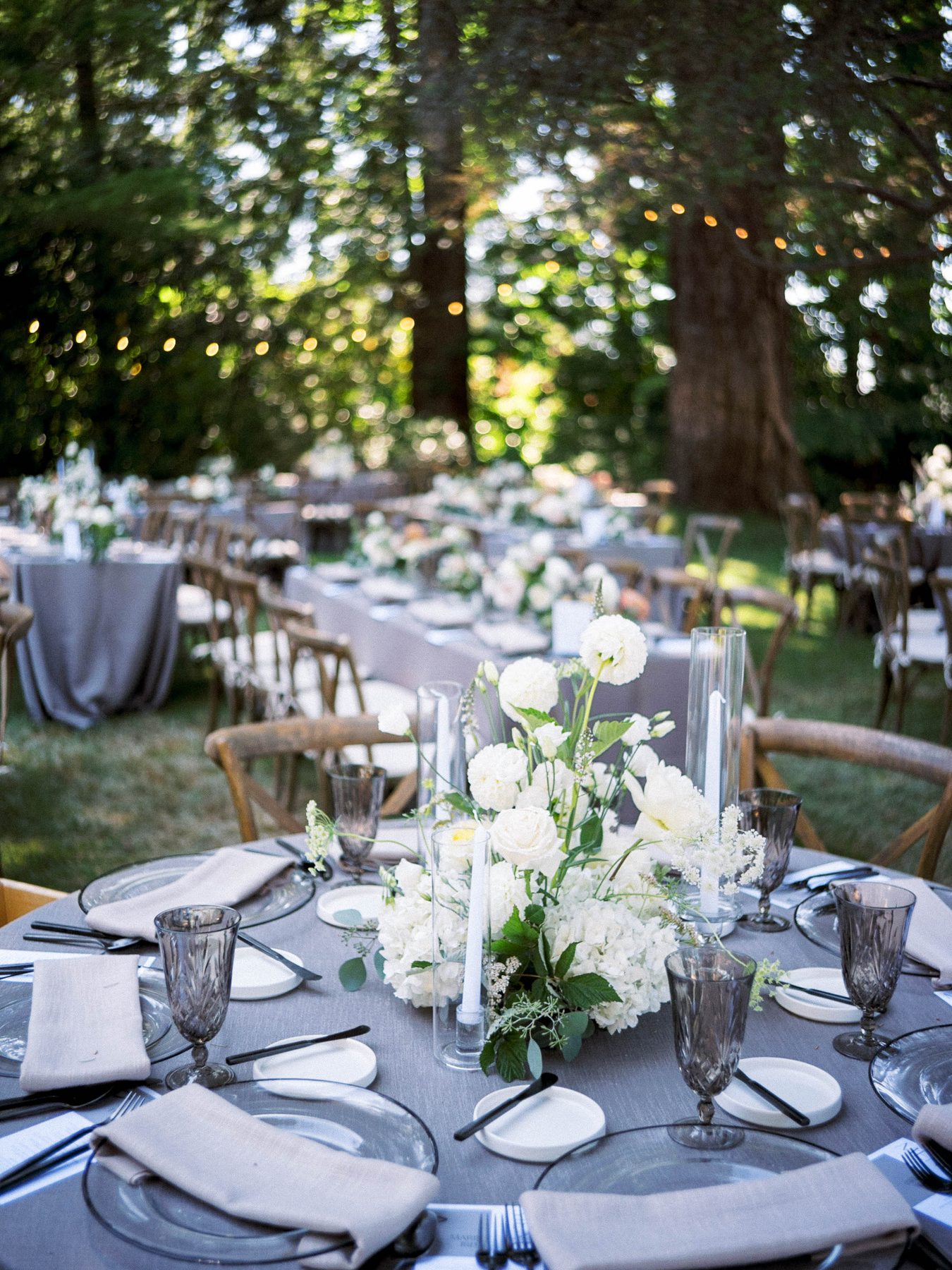 Wedding dinner tables set with flowers and glassware beneath trees.